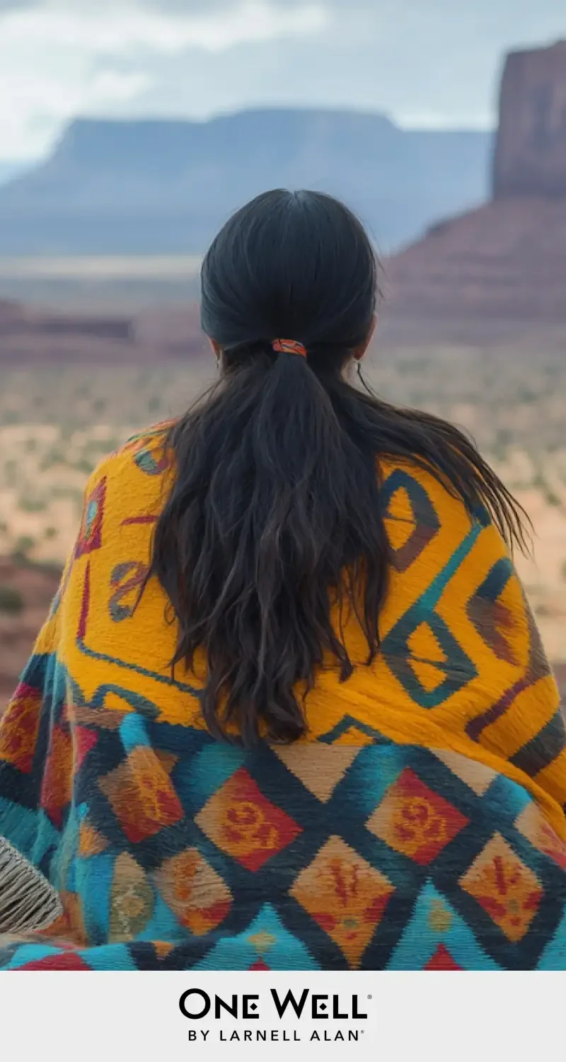 Person in colorful blanket gazes at vast desert landscape with mesas in the distance.