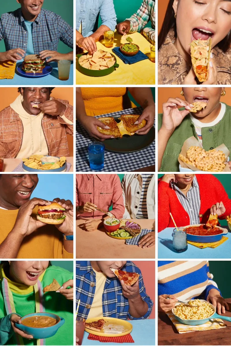 People enjoying various foods, including sandwiches, chips, burgers, mac and cheese, and pizza, at colorful tables.